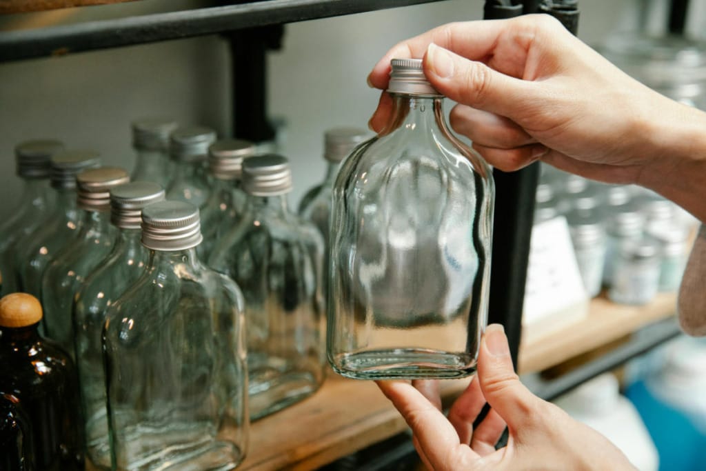 Person holding an empty glass bottle in front of a shelf with more empty glass bottles.