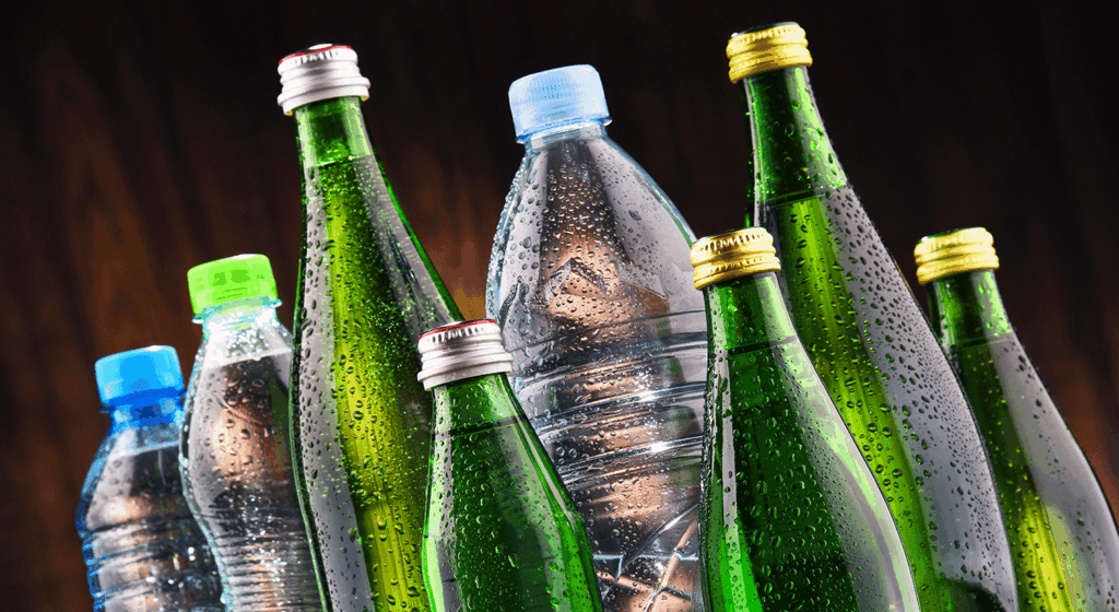 Assorted plastic and glass water bottles with condensation droplets against a dark background.